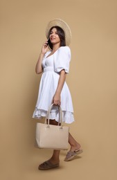 Photo of Young woman with stylish bag and smartphone on beige background