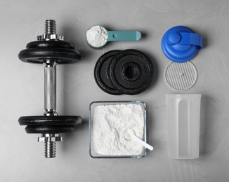 Flat lay composition with protein powder and dumbbell on grey background