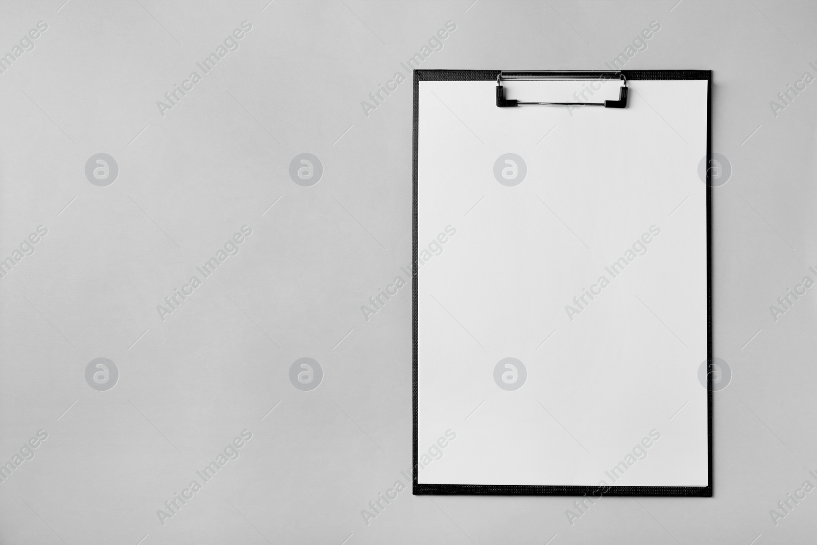 Photo of Black clipboard with sheet of blank paper on light grey background, top view. Space for text