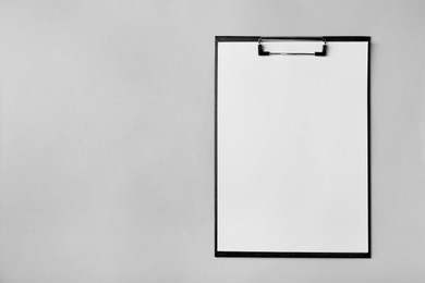 Black clipboard with sheet of blank paper on light grey background, top view. Space for text