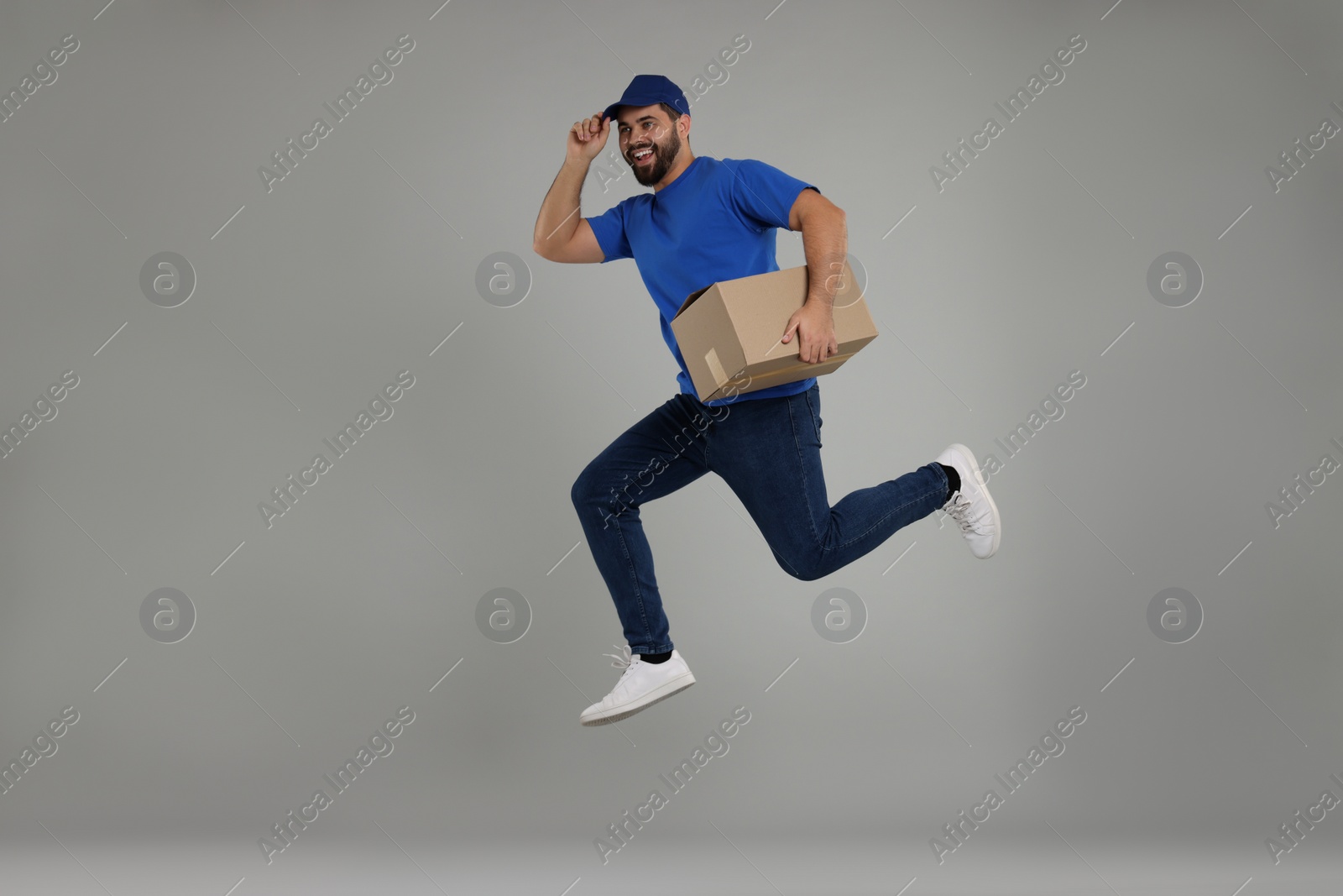 Photo of Happy young courier with parcel jumping on grey background