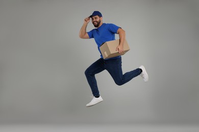 Happy young courier with parcel jumping on grey background