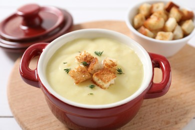 Photo of Tasty potato soup with croutons and rosemary in ceramic pot on white table, closeup