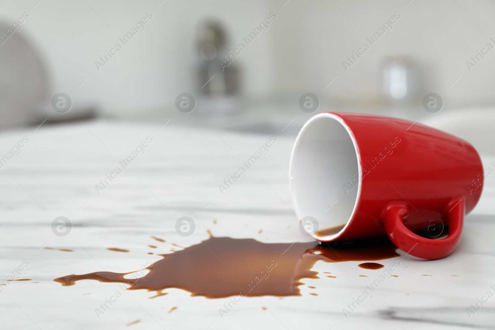 Photo of Overturned cup and spilled coffee on white marble table in kitchen, space for text