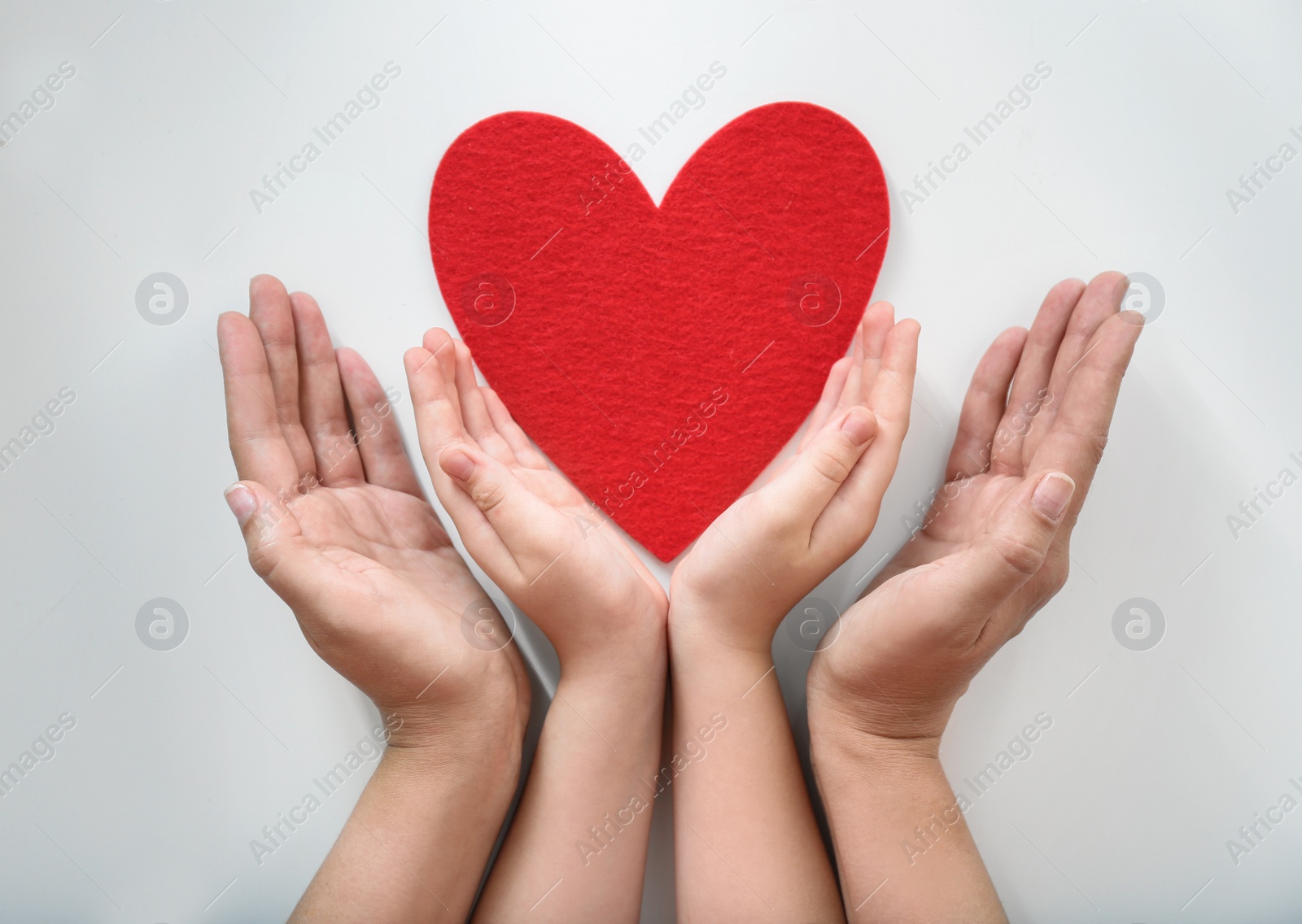 Photo of Young woman and child protecting red heart on light background, top view