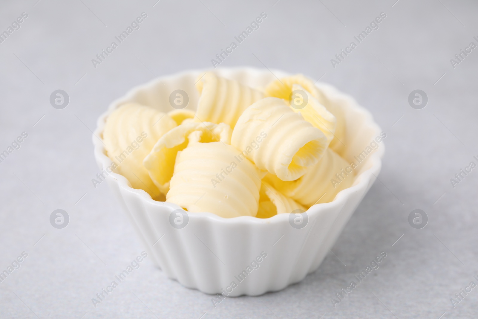 Photo of Tasty butter curls in bowl on light grey table, closeup