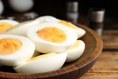 Photo of Cut hard boiled chicken eggs in wooden bowl on table, closeup