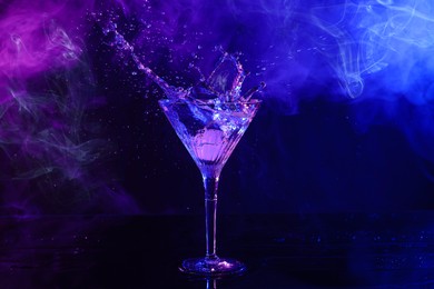 Photo of Martini splashing out of glass on table in neon lights