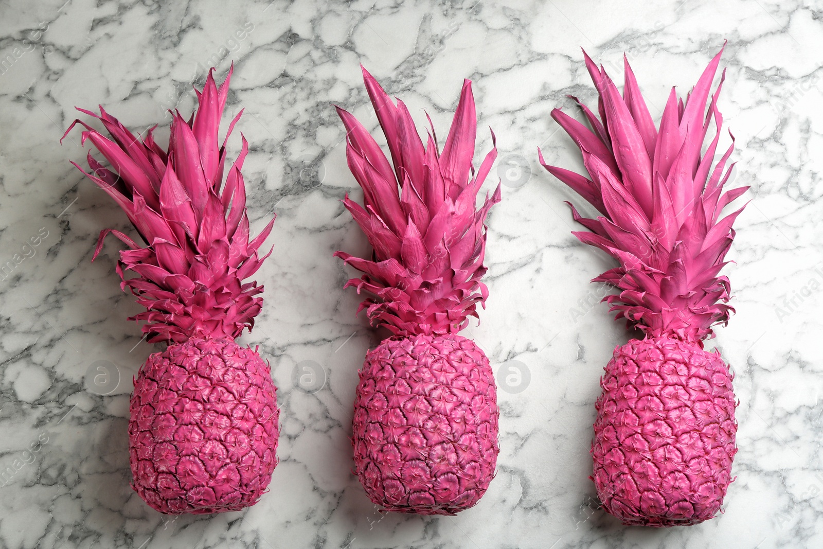 Photo of Pink pineapples on white marble background, flat lay. Creative concept