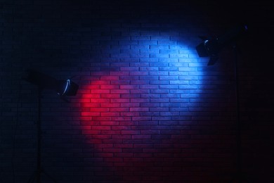 Photo of Bright blue and red spotlights near brick wall in dark room, space for text
