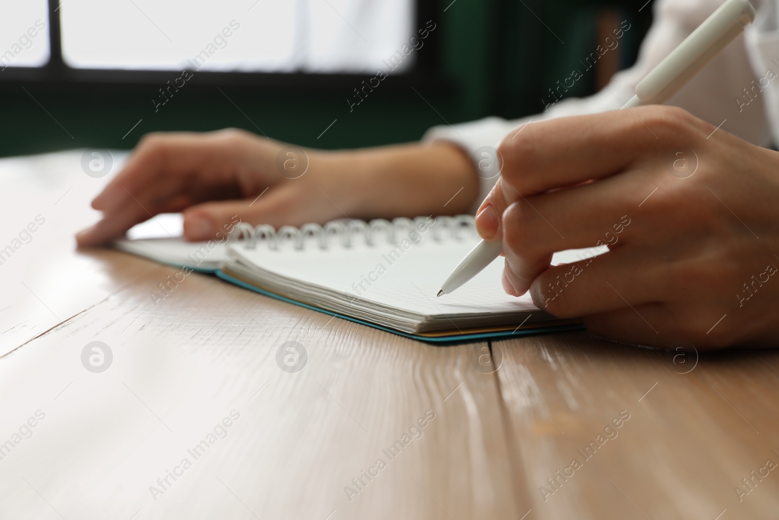 Photo of Left-handed woman writing in notebook at wooden table indoors, closeup