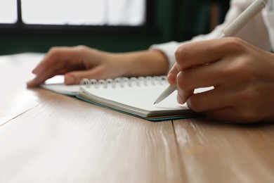 Photo of Left-handed woman writing in notebook at wooden table indoors, closeup