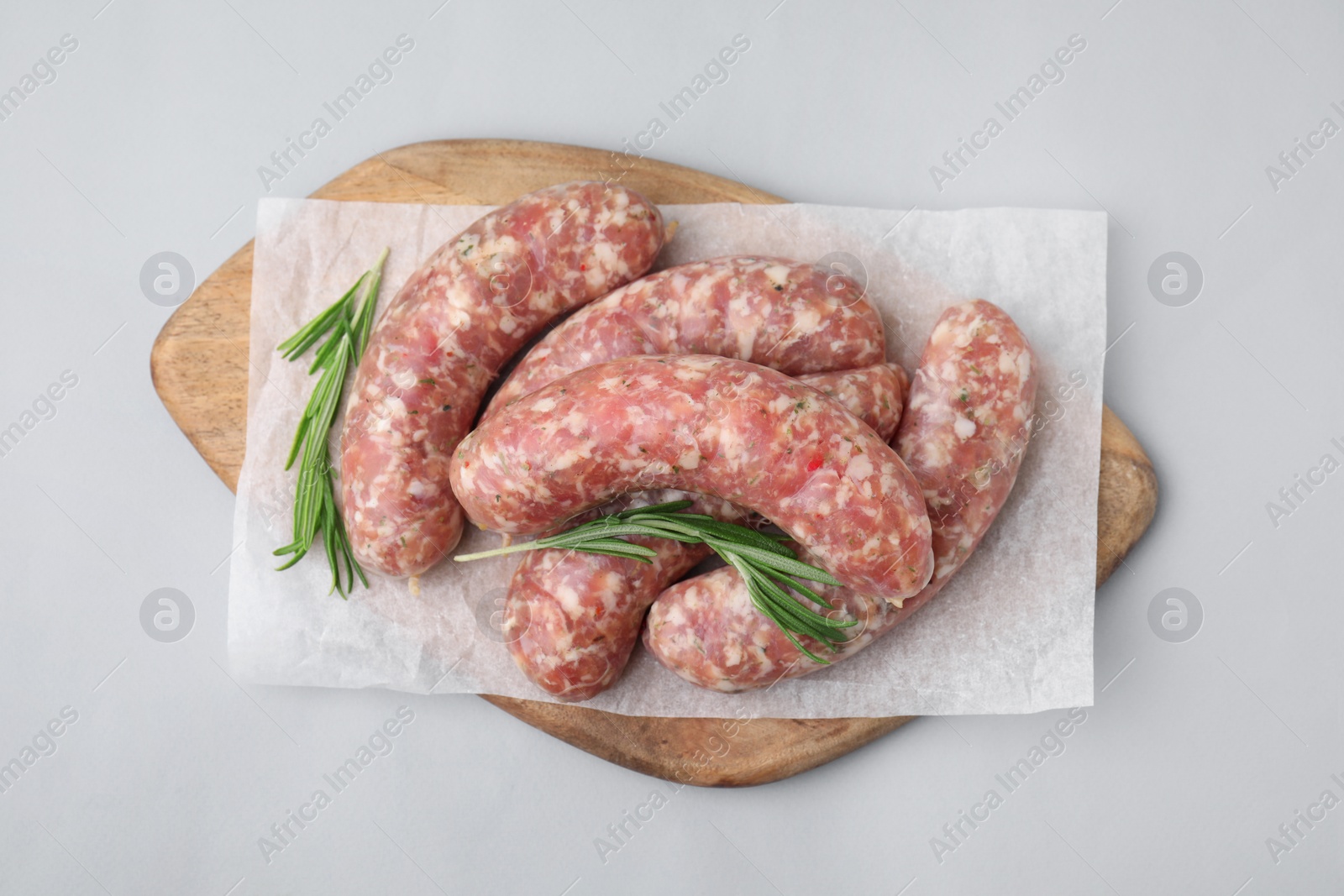 Photo of Wooden board with raw homemade sausages and rosemary on grey table, top view