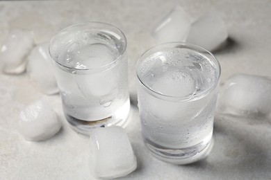 Photo of Shot glasses of vodka with ice cubes on light grey table, closeup