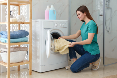 Young woman with clothes near washing machine in bathroom. Laundry day