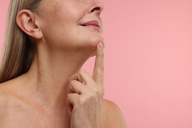 Mature woman with healthy skin on pink background, closeup. Space for text