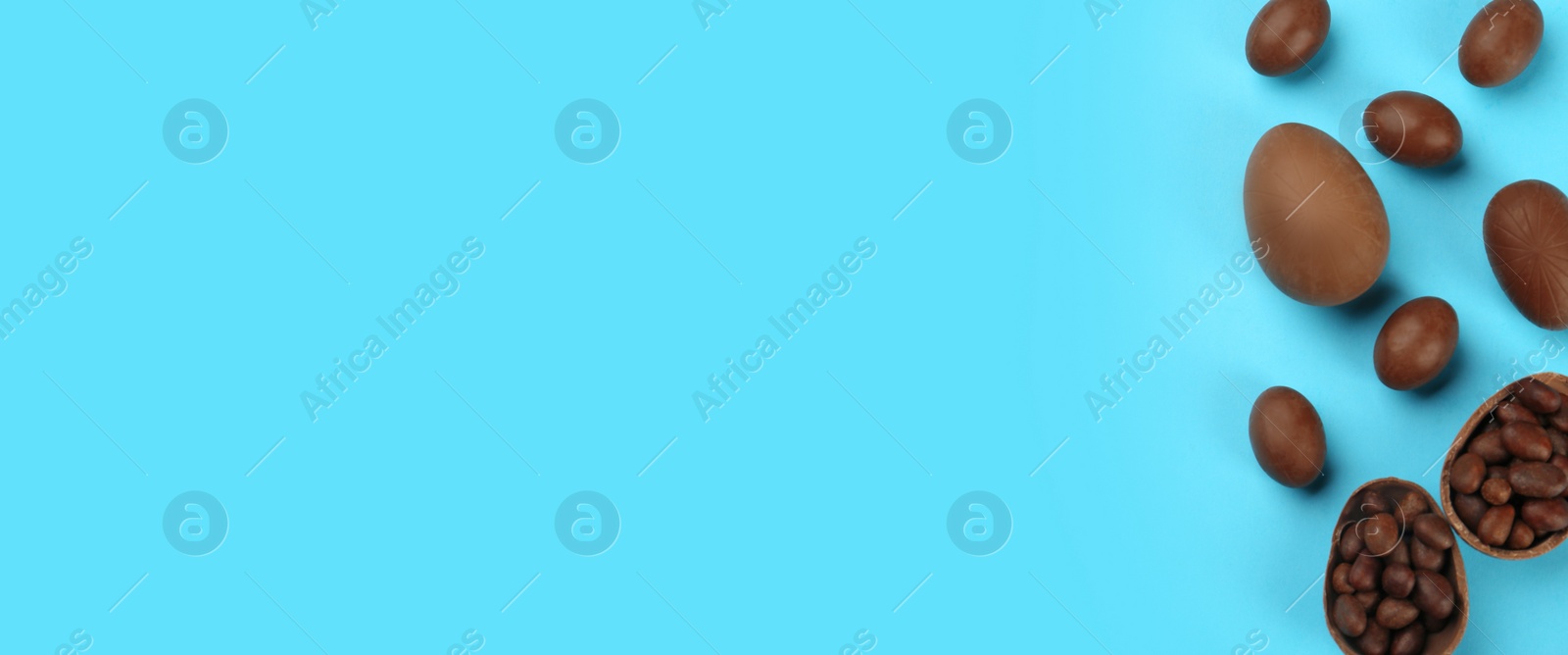 Image of Sweet chocolate eggs on light blue background, flat lay with space for text. Banner design