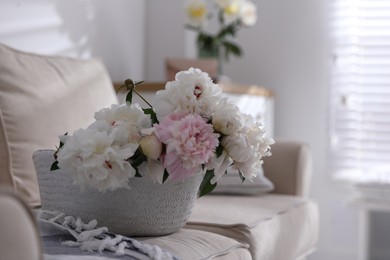 Bouquet of beautiful peony flowers in basket on sofa, closeup
