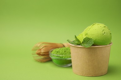 Paper cup with tasty matcha ice cream, bamboo whisk and powder on light green background. Space for text