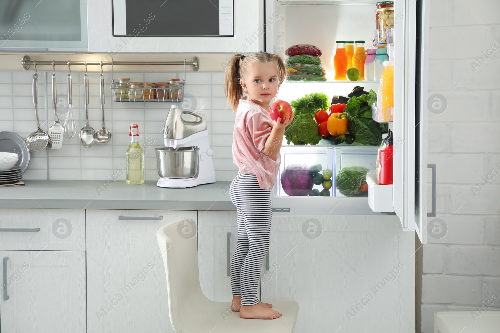 Photo of Cute girl taking apple out of refrigerator in kitchen
