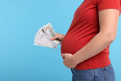 Surrogate mother. Pregnant woman with dollar banknotes on light blue background, closeup. Space for text