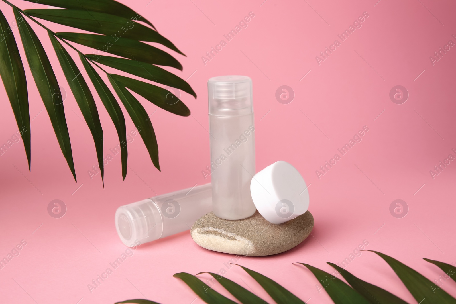 Photo of Cosmetic products, stone and palm leaves on pink background