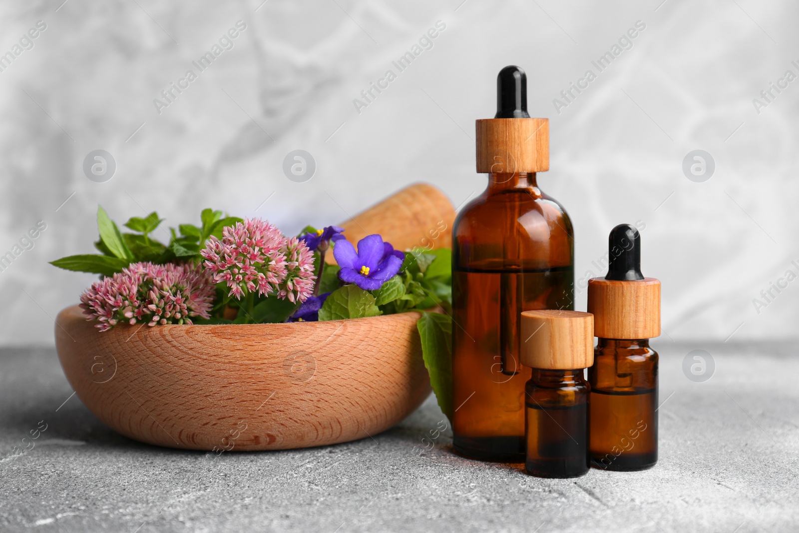 Photo of Glass bottles of essential oil and mortar with different wildflowers on light grey table