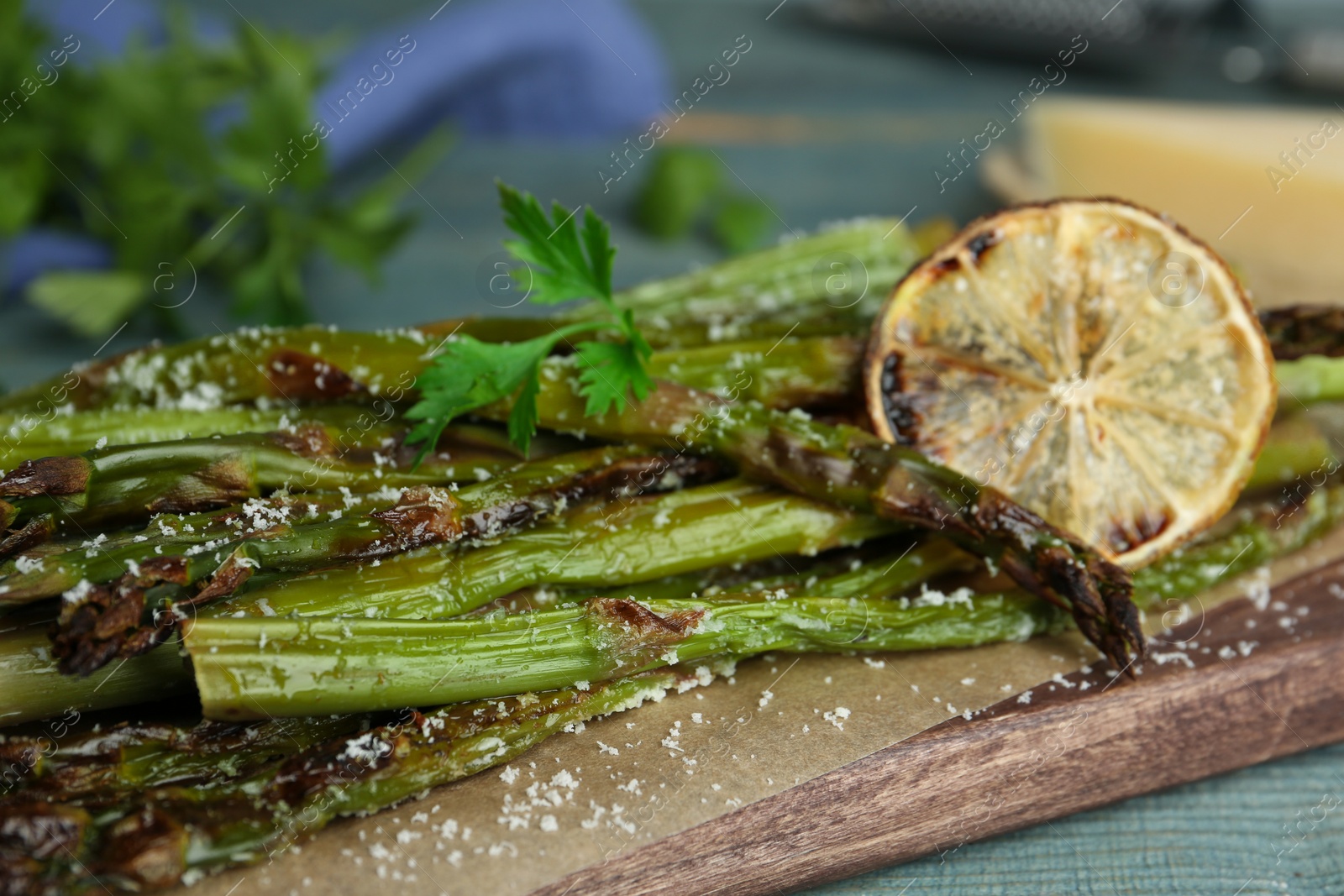 Photo of Oven baked asparagus served with lemon and parsley on blue wooden board, closeup