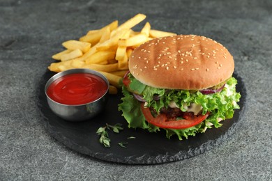 Photo of Delicious burger with beef patty, tomato sauce and french fries on grey table
