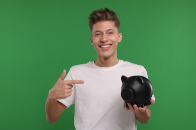 Photo of Happy man pointing at piggy bank on green background