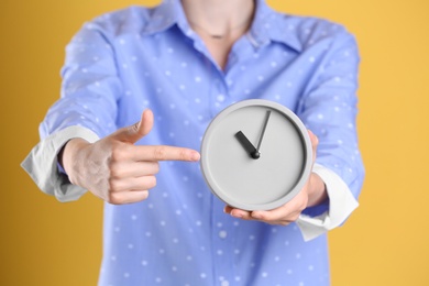 Young woman holding alarm clock on color background. Time concept