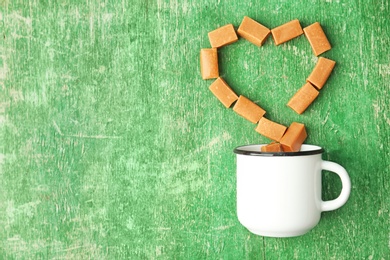 Photo of Delicious caramel candies and mug on wooden background, top view