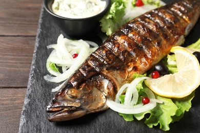 Slate plate with delicious grilled fish and sauce on table, closeup