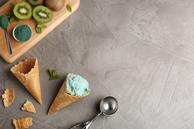 Photo of Flat lay composition with delicious spirulina ice cream cones and scoop on grey background. Space for text