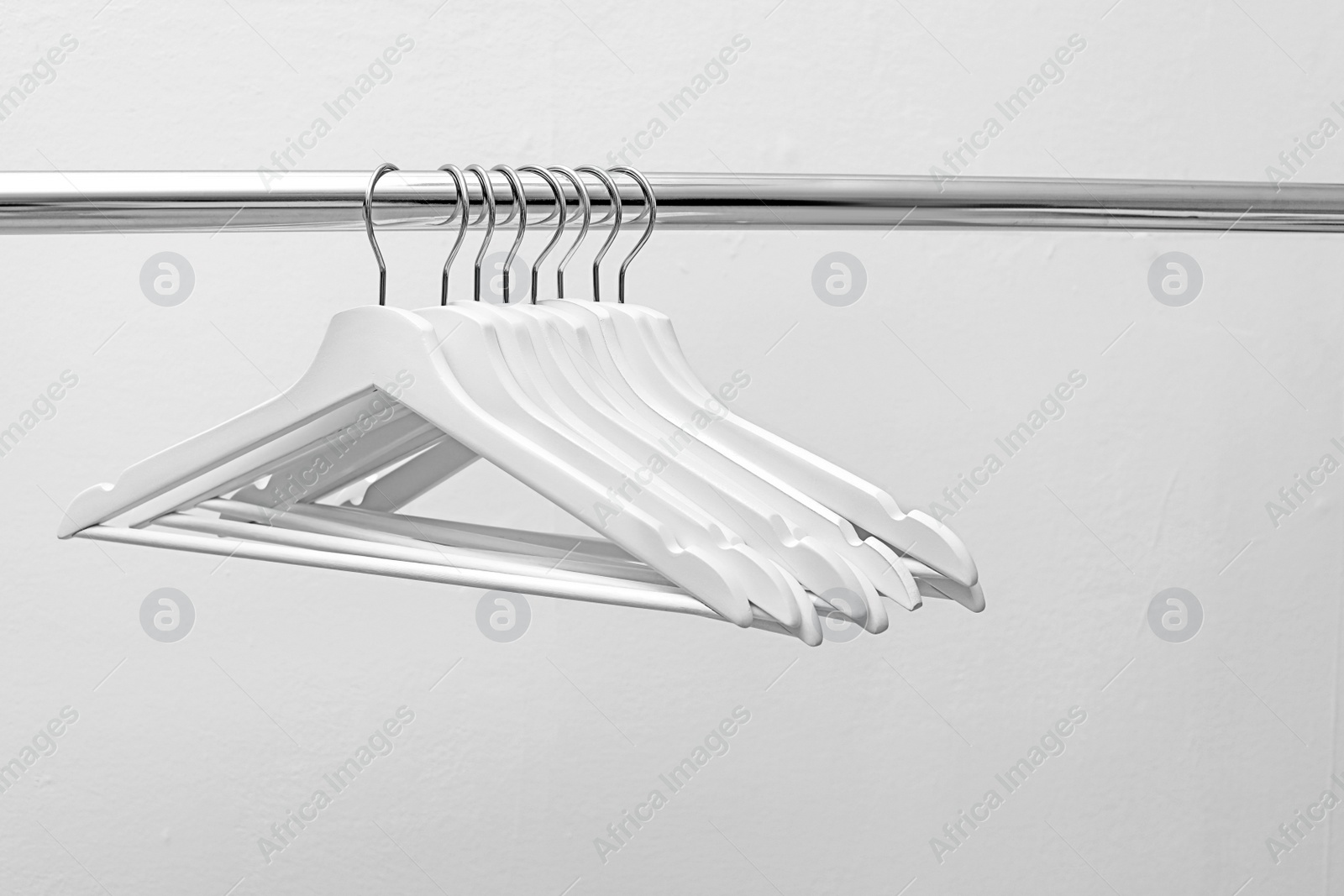 Photo of Clothes hangers on metal rail against light background