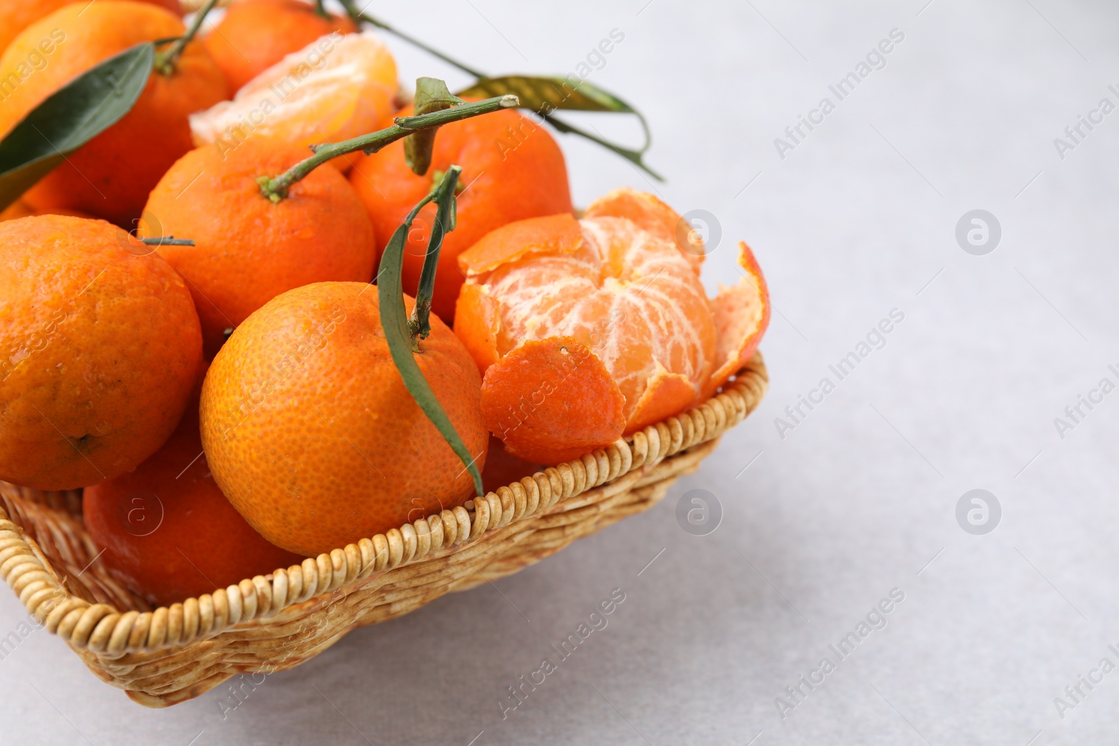Photo of Fresh ripe tangerines with green leaves in wicker basket on white table, closeup. Space for text