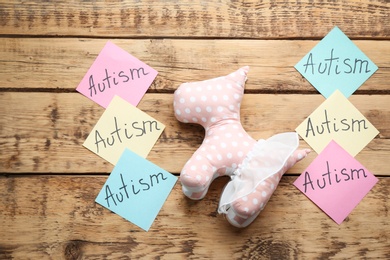 Sticky notes with word "Autism" and toy on wooden background, flat lay