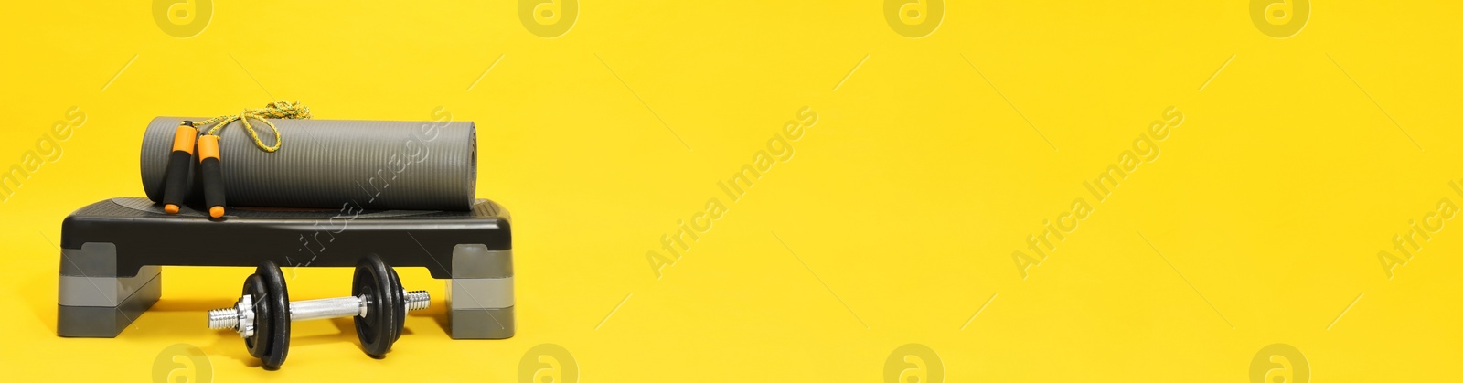 Image of Step platform, dumbbell, mat and jump rope on yellow background, space for text. Banner design