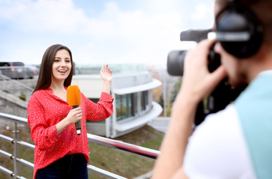 Young journalist and video operator working on city street