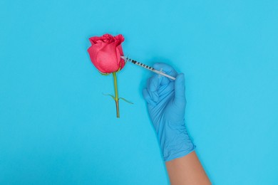 Doctor making injection to rose on light blue background, top view