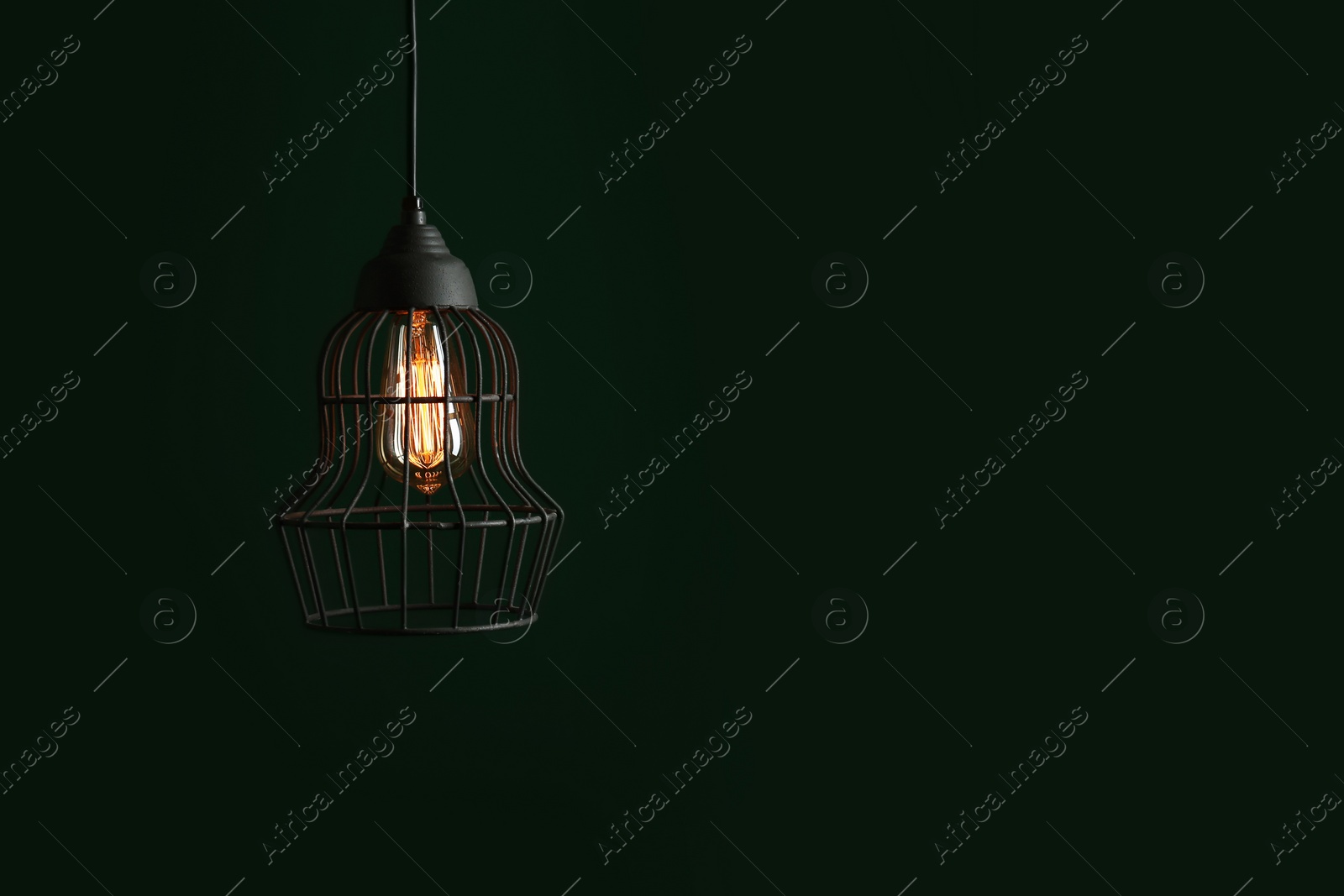 Photo of Hanging lamp bulb in chandelier against green background, space for text