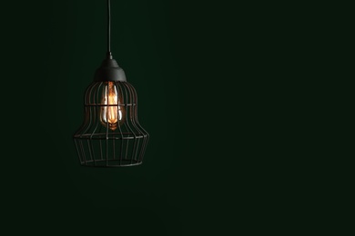Hanging lamp bulb in chandelier against green background, space for text