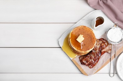 Delicious pancakes with maple syrup, butter and fried bacon on white wooden table, flat lay. Space for text