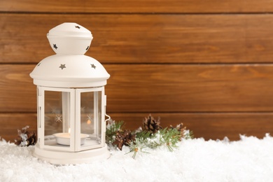 Photo of Christmas lantern with burning candle and fir tree branch on snow. Space for text