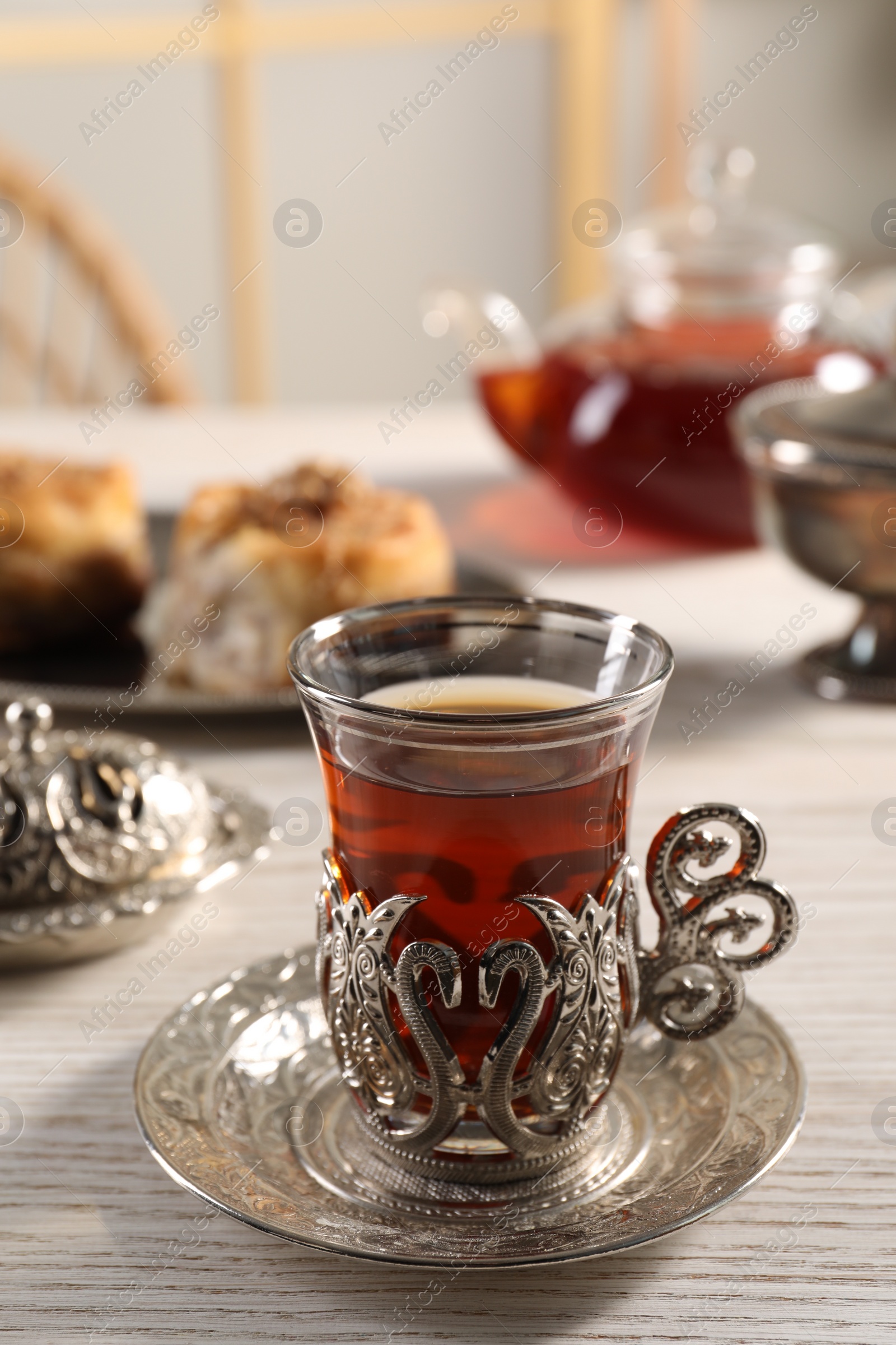 Photo of Glass of traditional Turkish tea in vintage holder on white wooden table