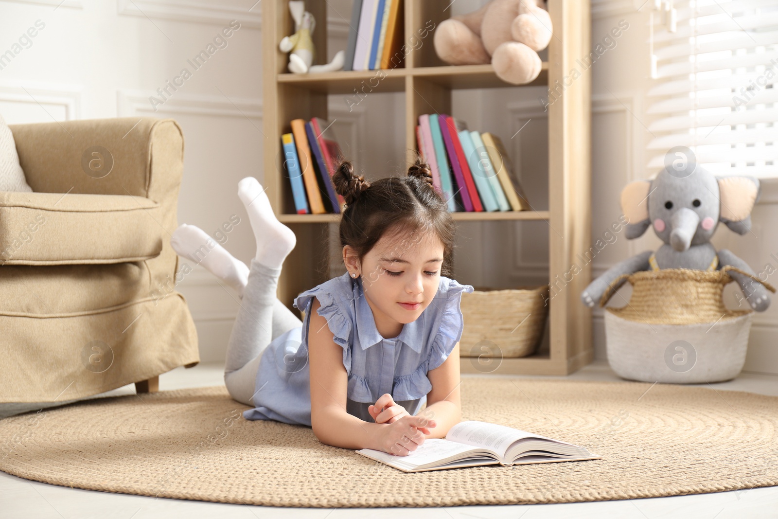 Photo of Little girl reading book on floor at home