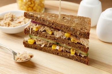 Photo of Delicious sandwich with tuna, vegetables and spoon of fish meat on wooden board, closeup