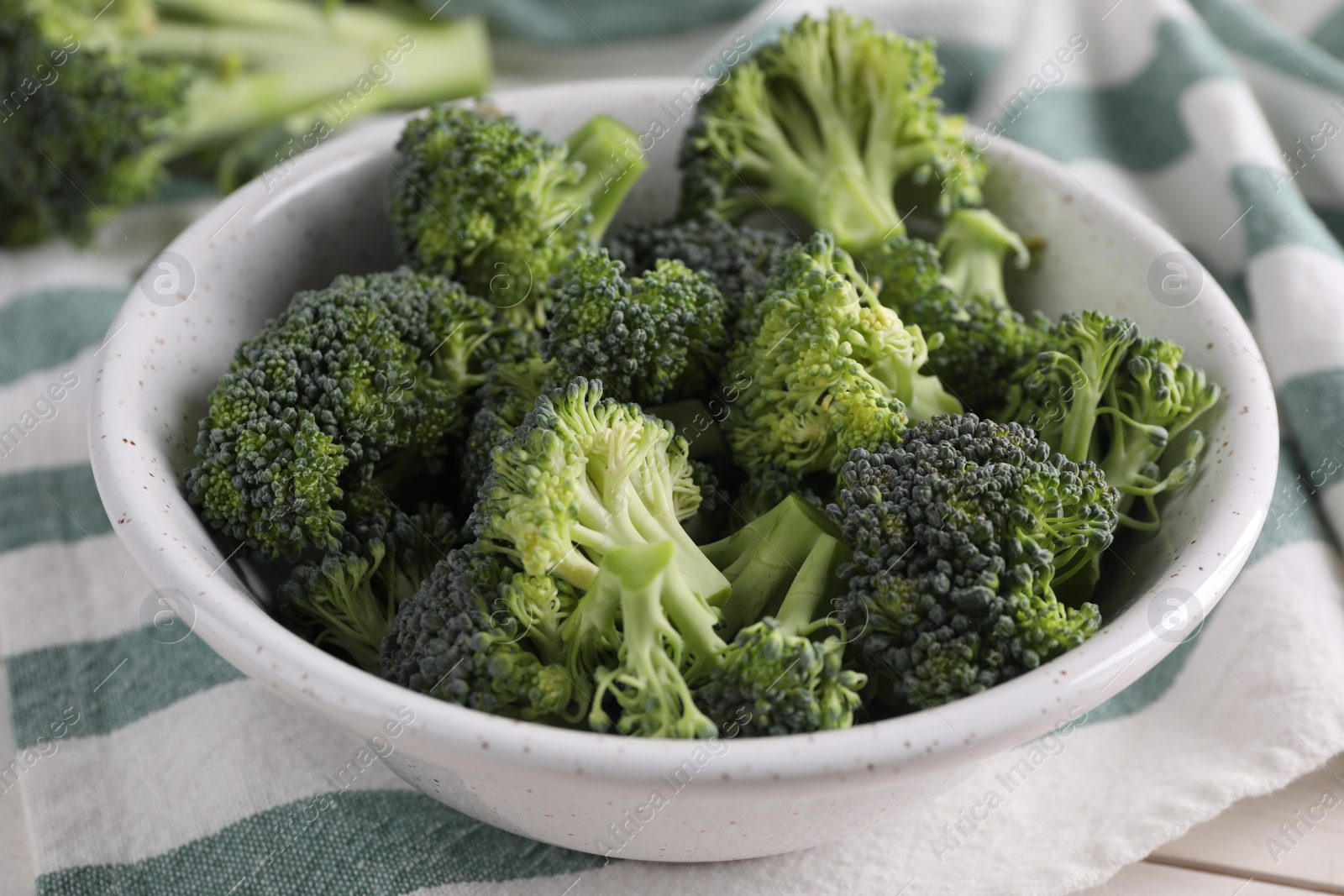 Photo of Bowl with fresh raw broccoli on white table, closeup