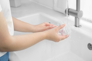 Photo of Woman washing baby bottle under stream of water in kitchen, closeup