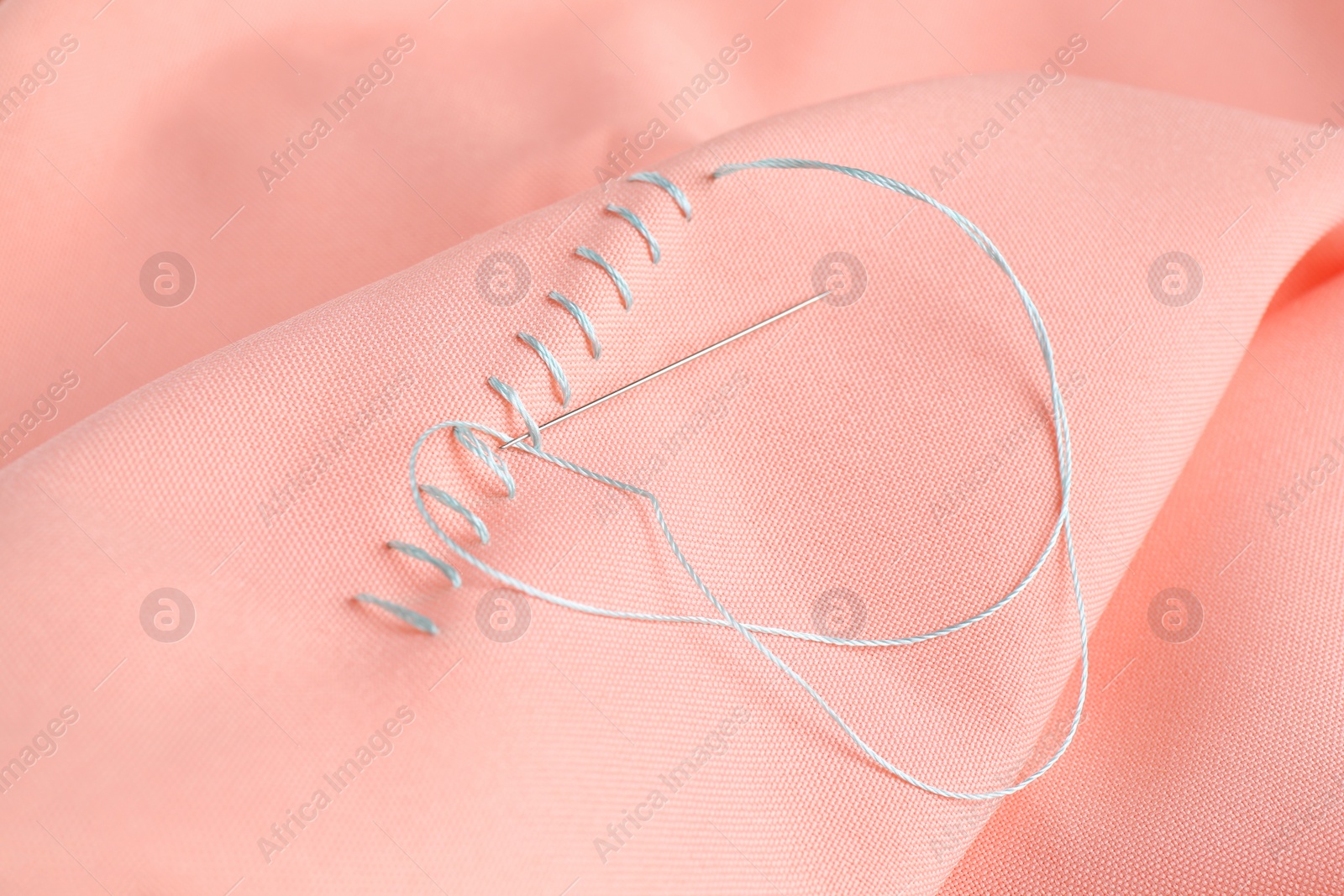 Photo of Sewing needle with thread and stitches on coral cloth, closeup